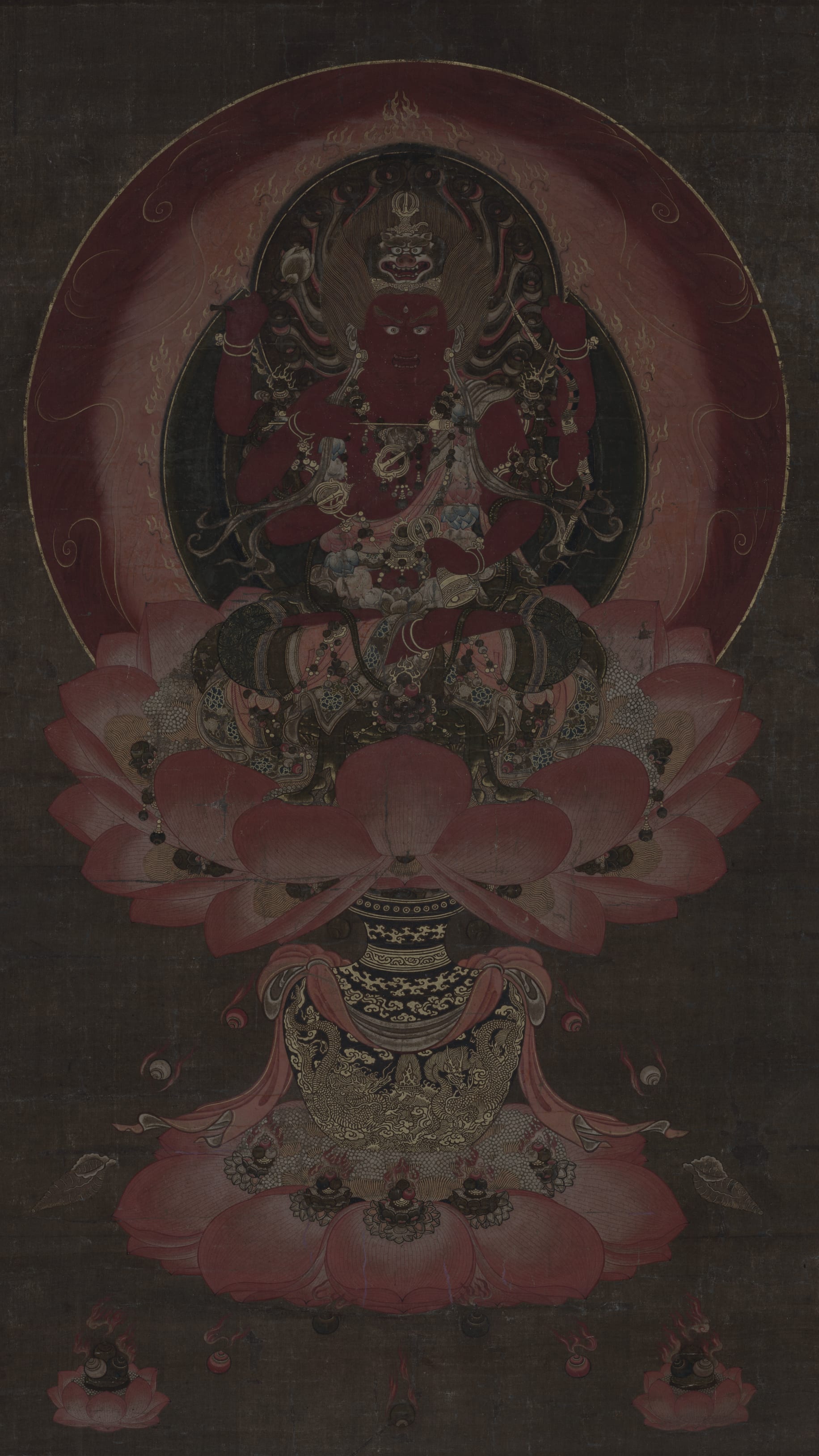 Dark moody vertical iPhone background from a Japanese painting: fierce red Buddhist deity with multiple arms seated on a lotus throne, deep crimson circular halo, large pink lotus petals, dark brown ground
