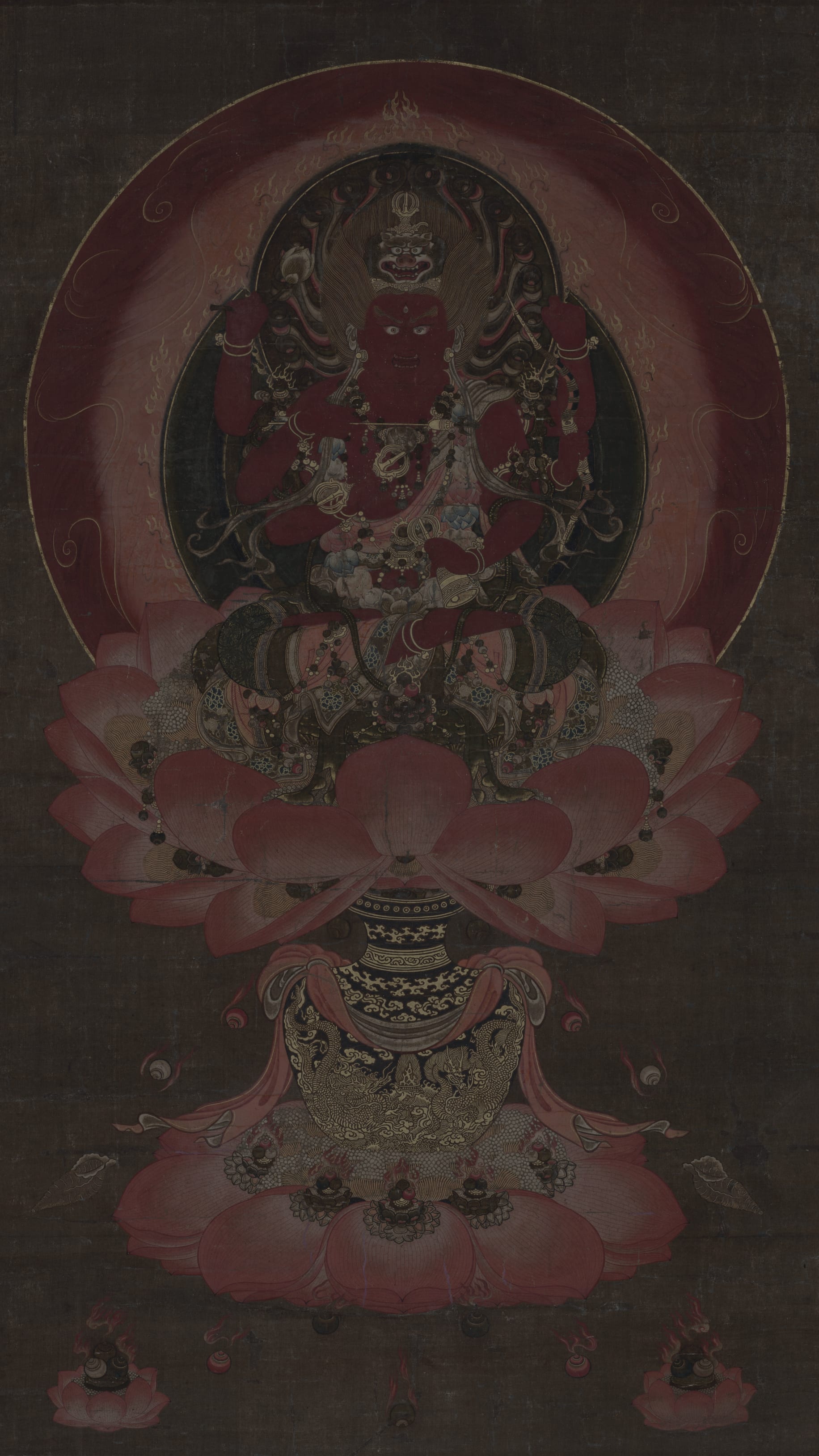 Dark moody vertical iPhone background from a Japanese painting: fierce red Buddhist deity with multiple arms seated on a lotus throne, deep crimson circular halo, large pink lotus petals, dark brown ground