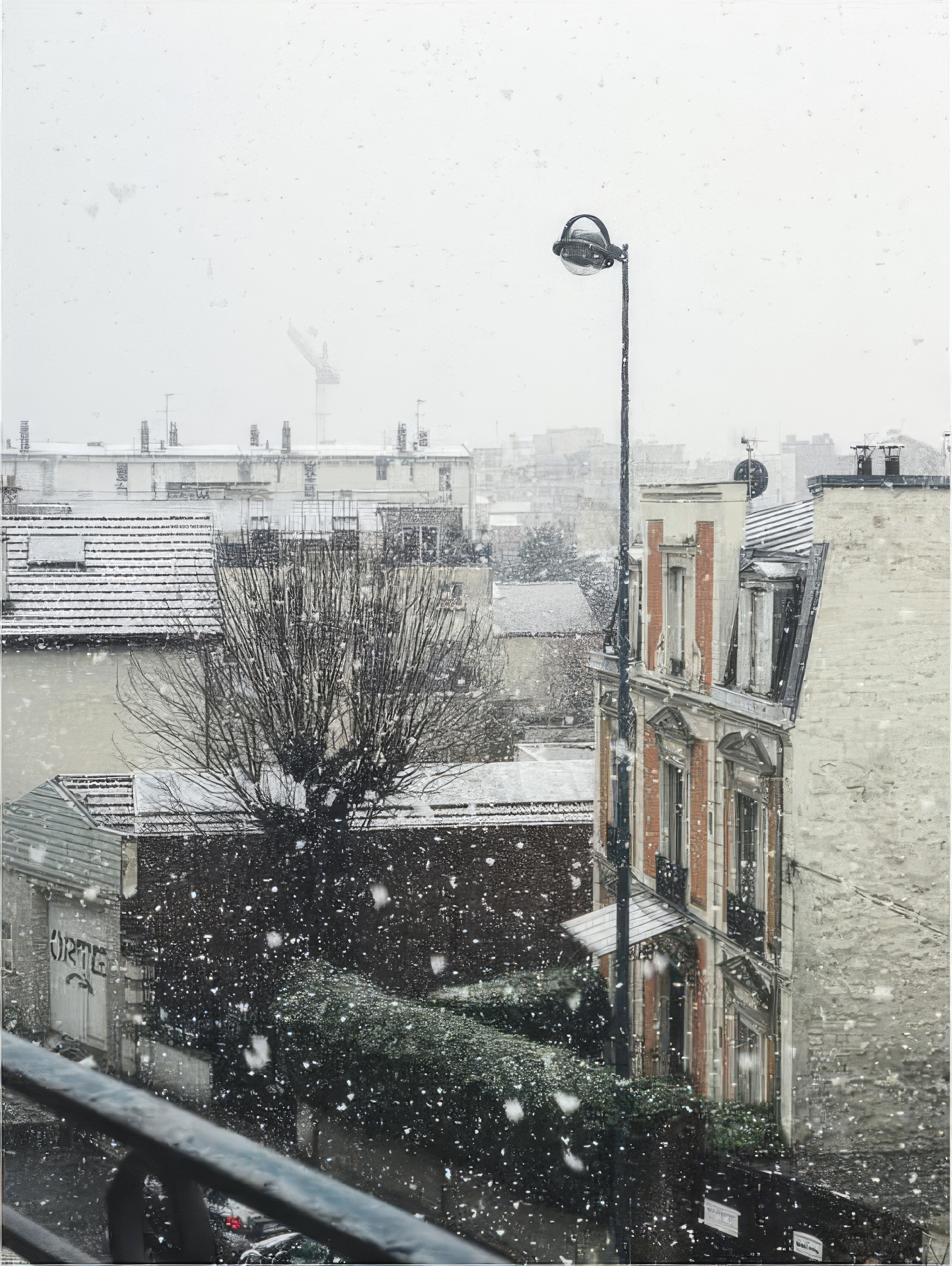 Phone wallpaper photo: snow falling over a row of rooftops, seen from a balcony railing