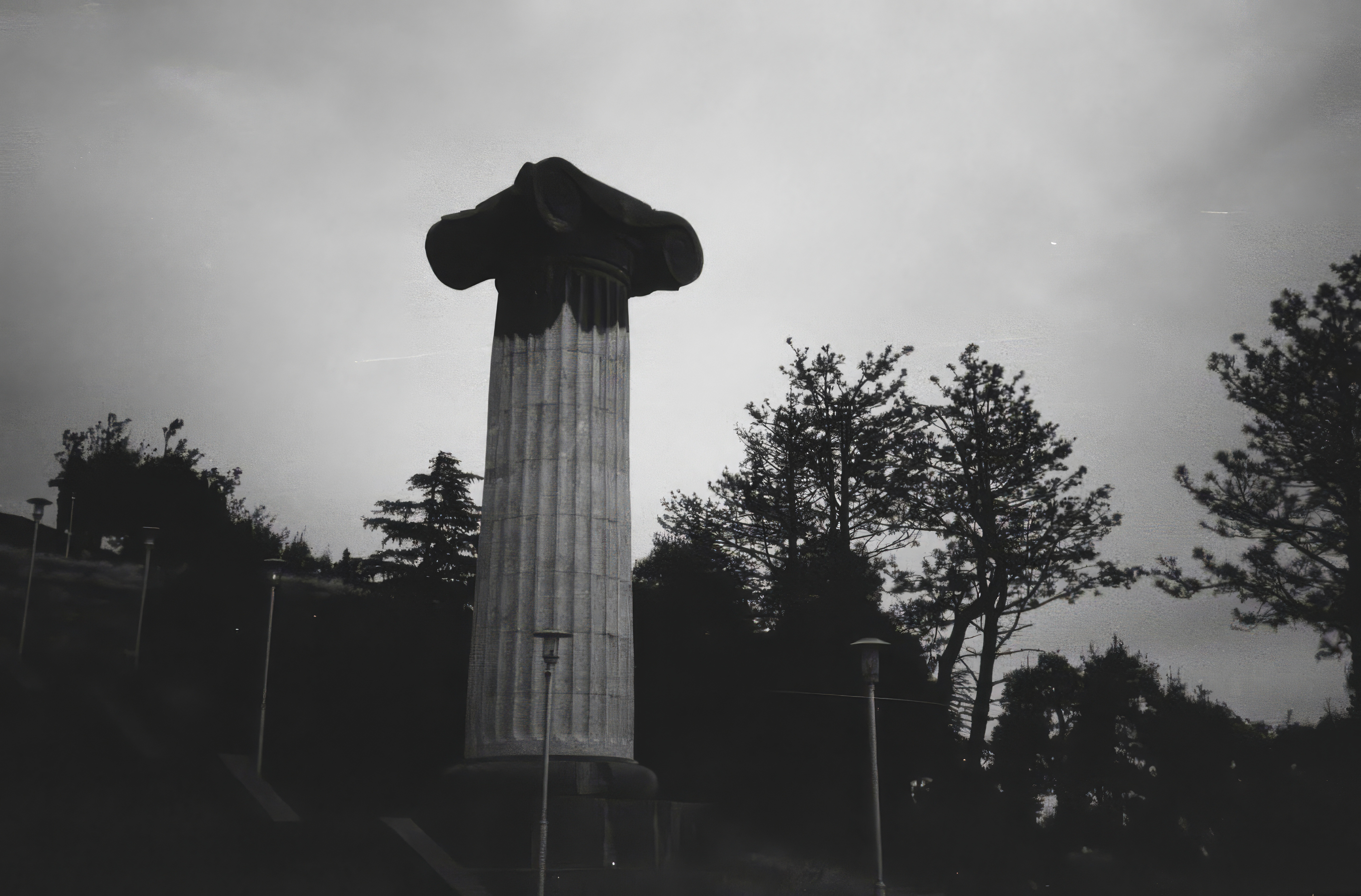 Desktop wallpaper photo: a stone column silhouetted against an overcast sky above a hedge